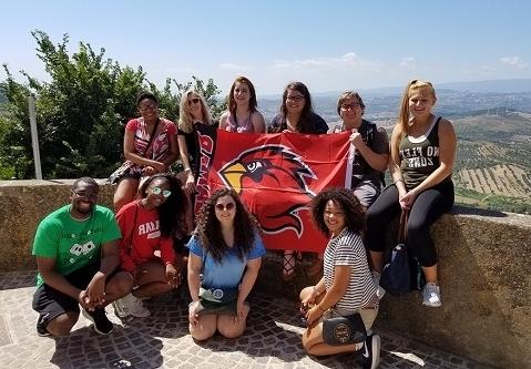 Psychology in Italy, students sitting on ledge holding flag with LU Cardinal logo